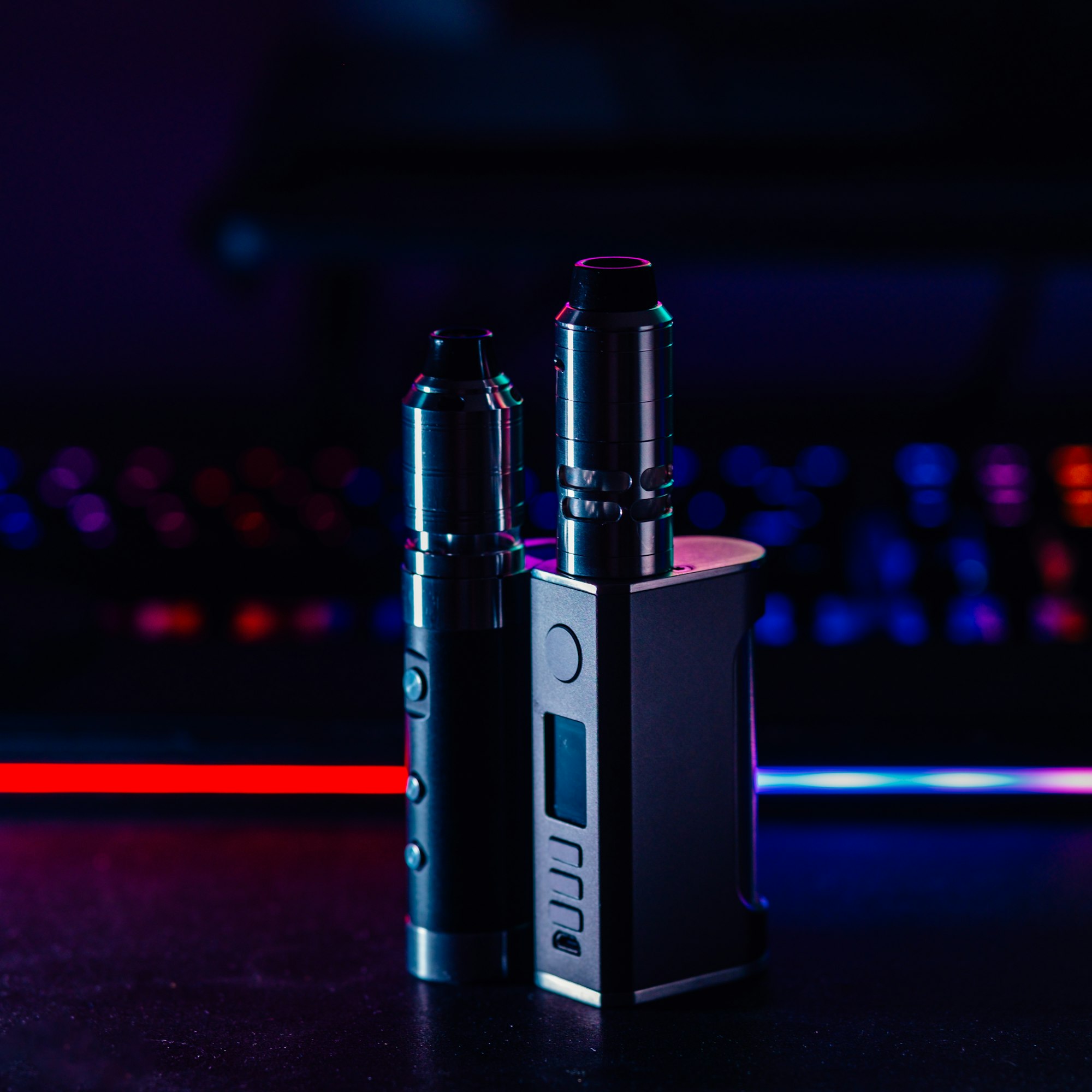 A dark vape device lit from behind against black